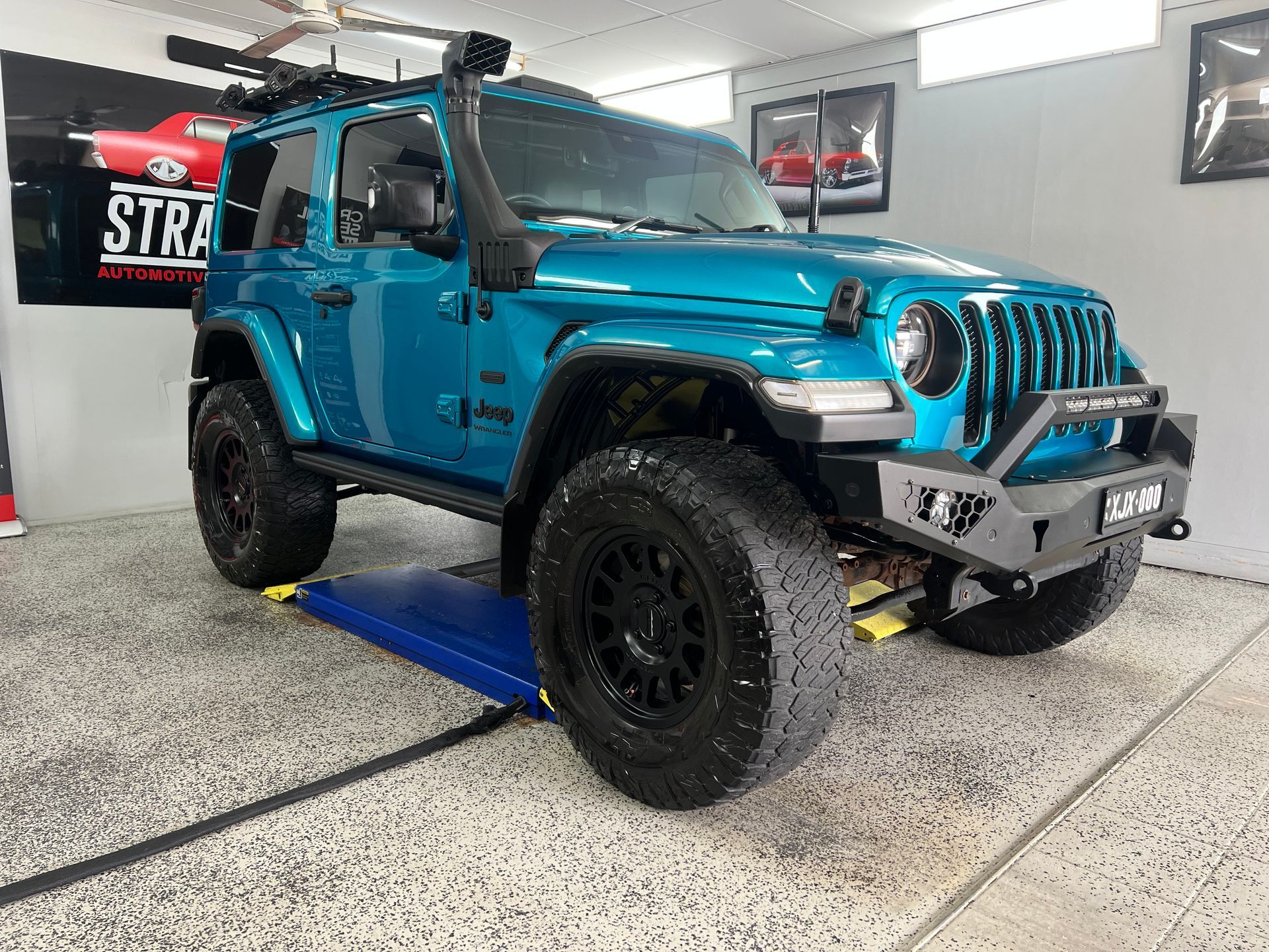 Bright Blue Off-Road Jeep in A Garage, Lifted on A Blue Ramp — Straightline Detailing Cairns in Bungalow, QLD