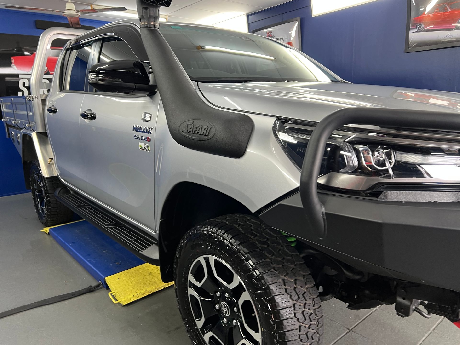 White Pickup Truck on A Blue-And-Yellow Automotive Lift — Straightline Detailing Cairns in Bungalow, QLD