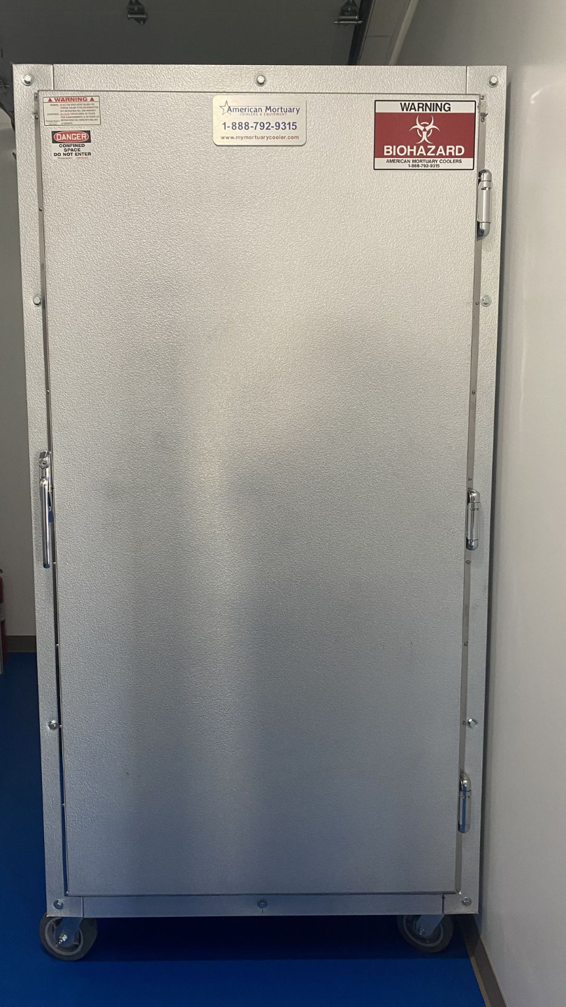 Silver metal cabinet on wheels, against a white wall and blue floor.