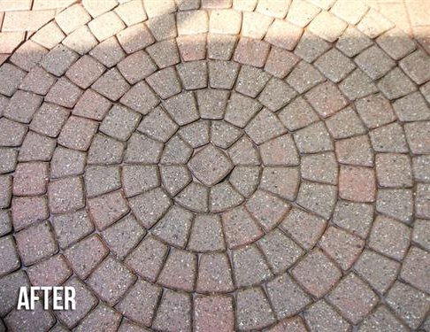 Circular brick patio, cleaned. Pattern of concentric rings with reddish-brown and tan bricks, in sunlight.