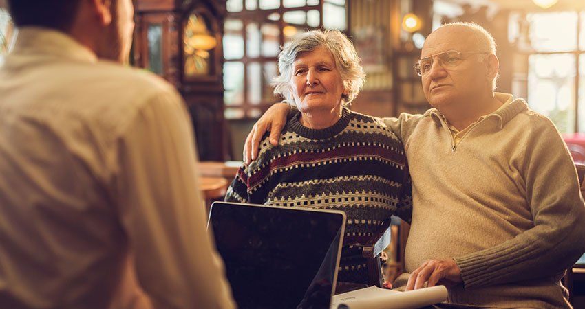 Two older people talk to a younger man with a laptop