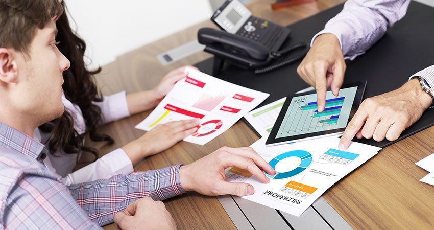 3 people look over statistics and charts on papers and on a tablet