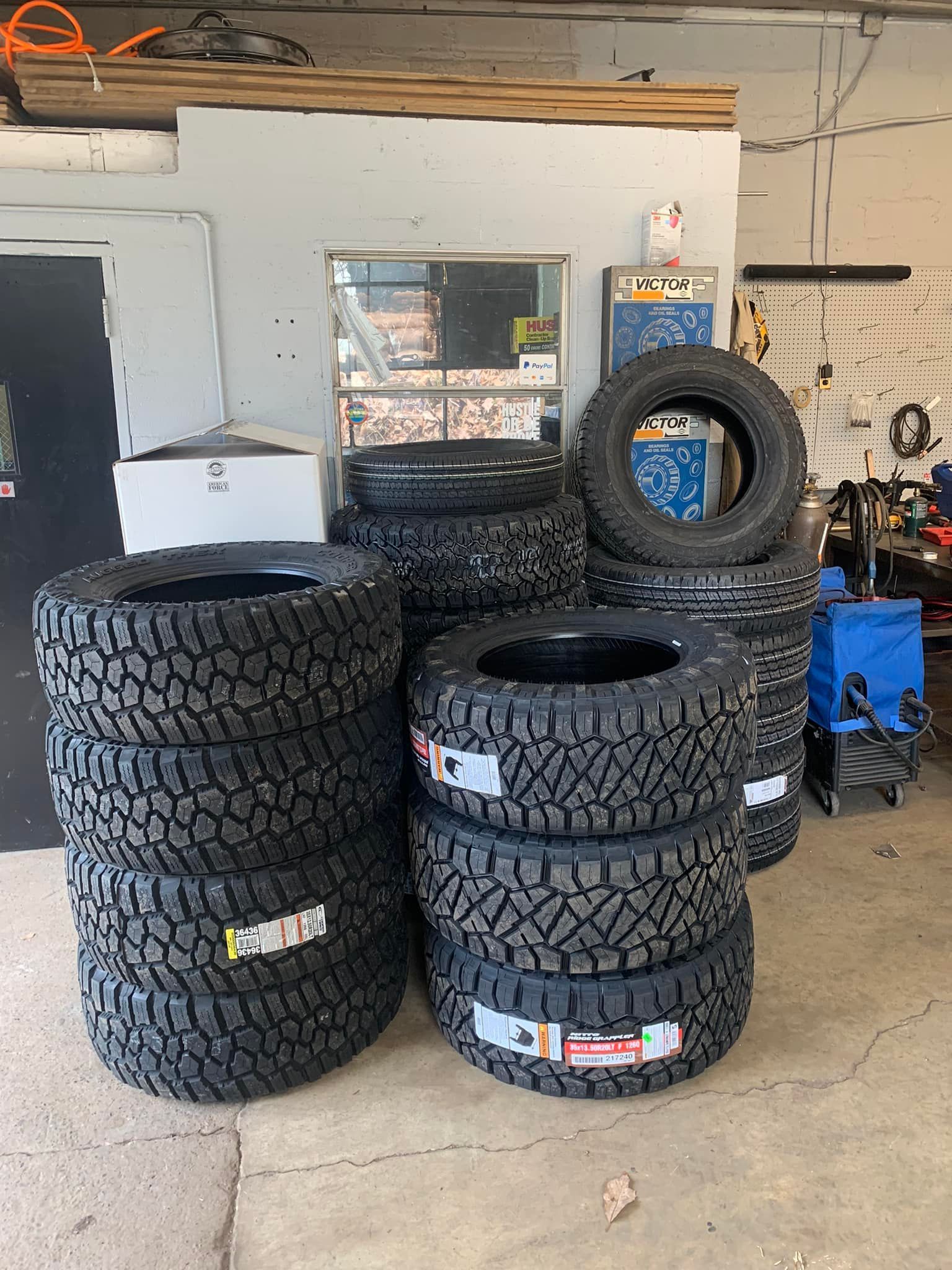 A bunch of tires are stacked on top of each other in a garage. | DirtLife Fab & 4x4