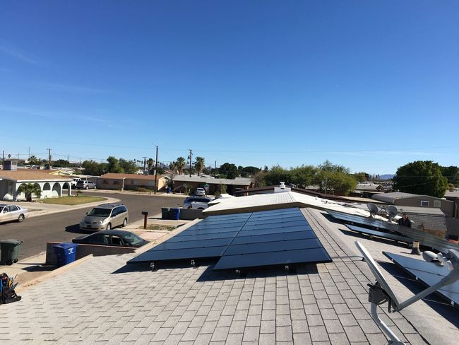 Solar panels installed on a rooftop under a clear blue sky, with a neighborhood visible in the distance.