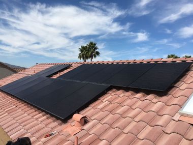 Black solar panels mounted on a red tile roof under a partly cloudy sky