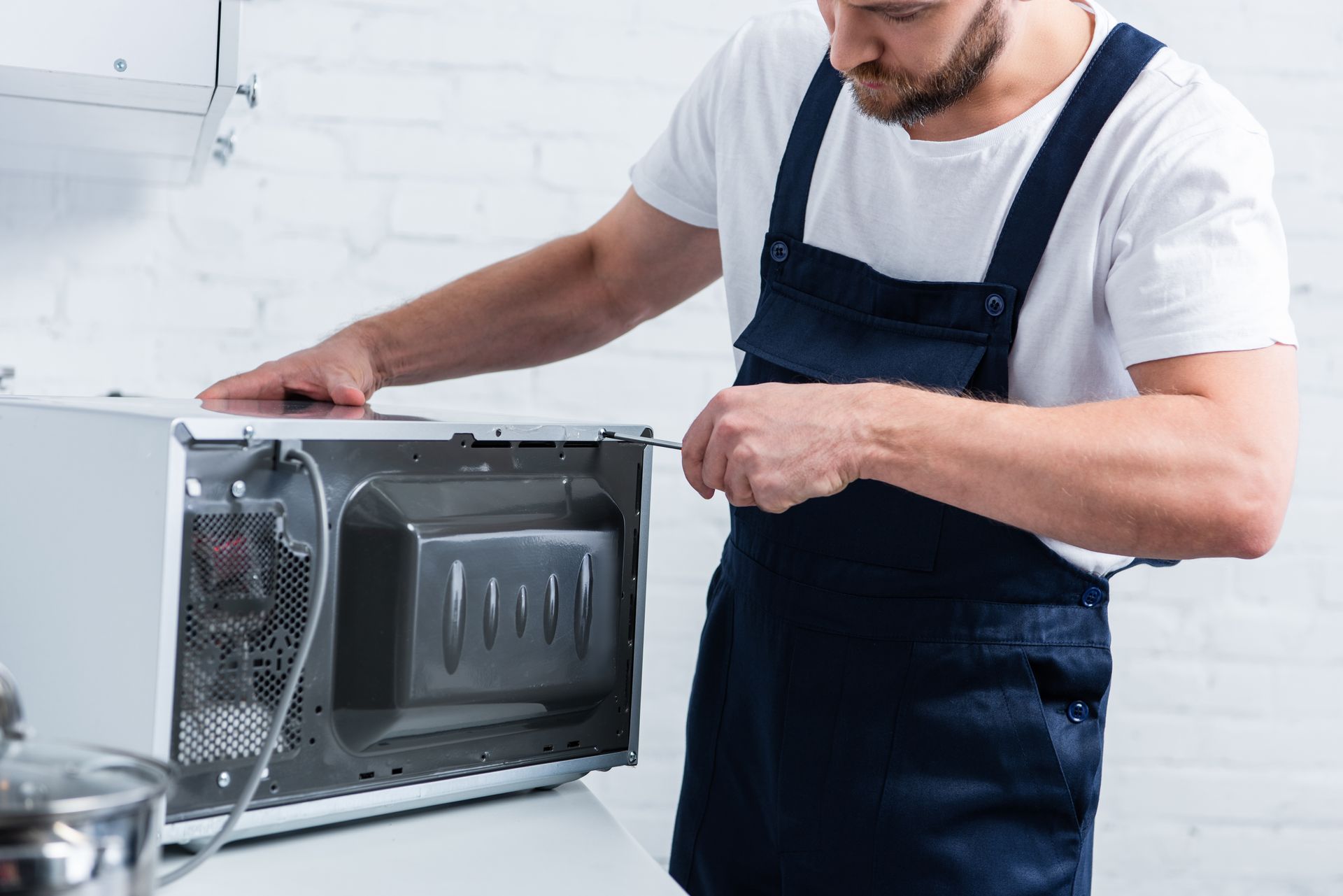 Technician in a navy apron inspecting a microwave oven on a white countertop