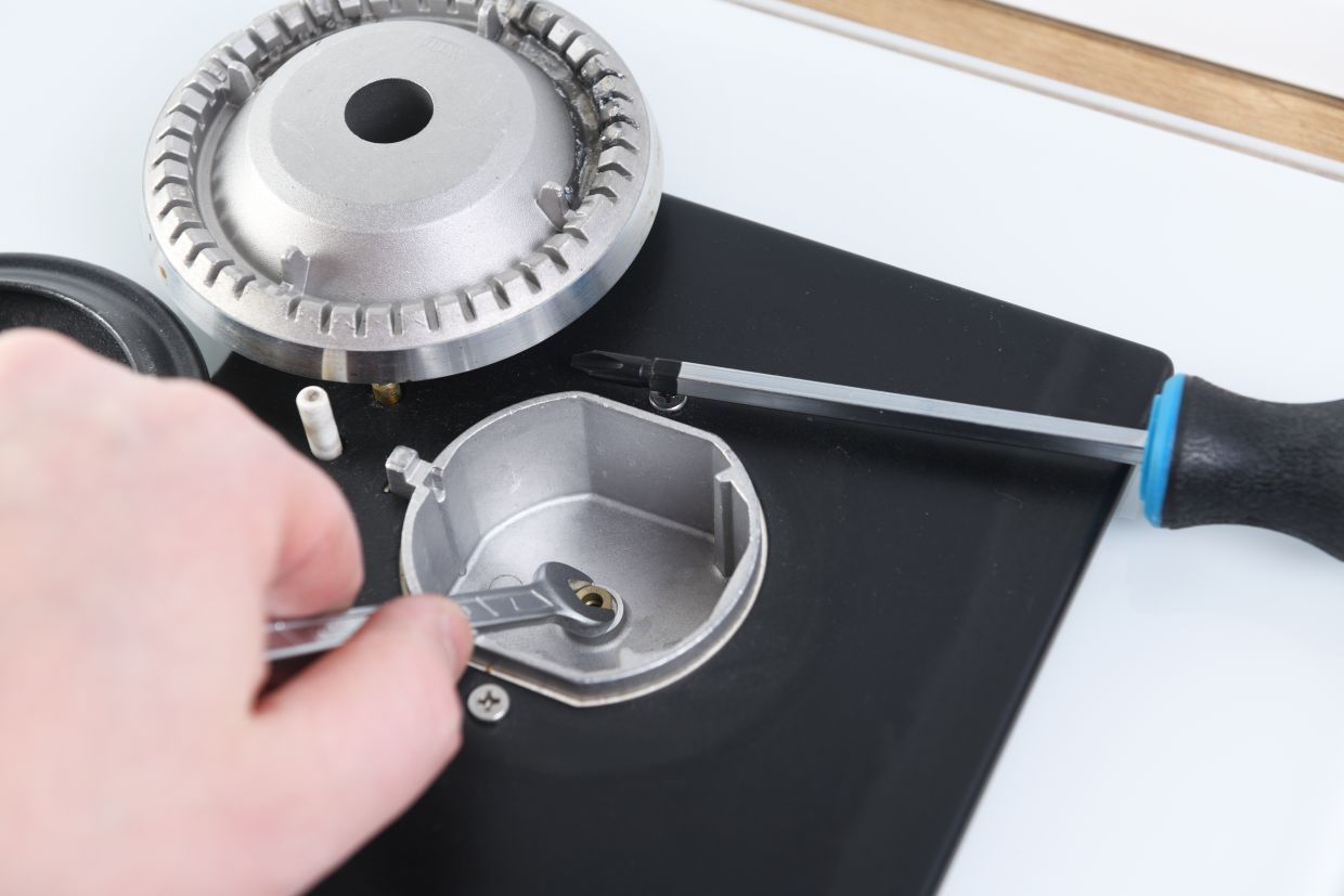 Hand turning a gas stove burner knob beside a large pan and blue-handled knife