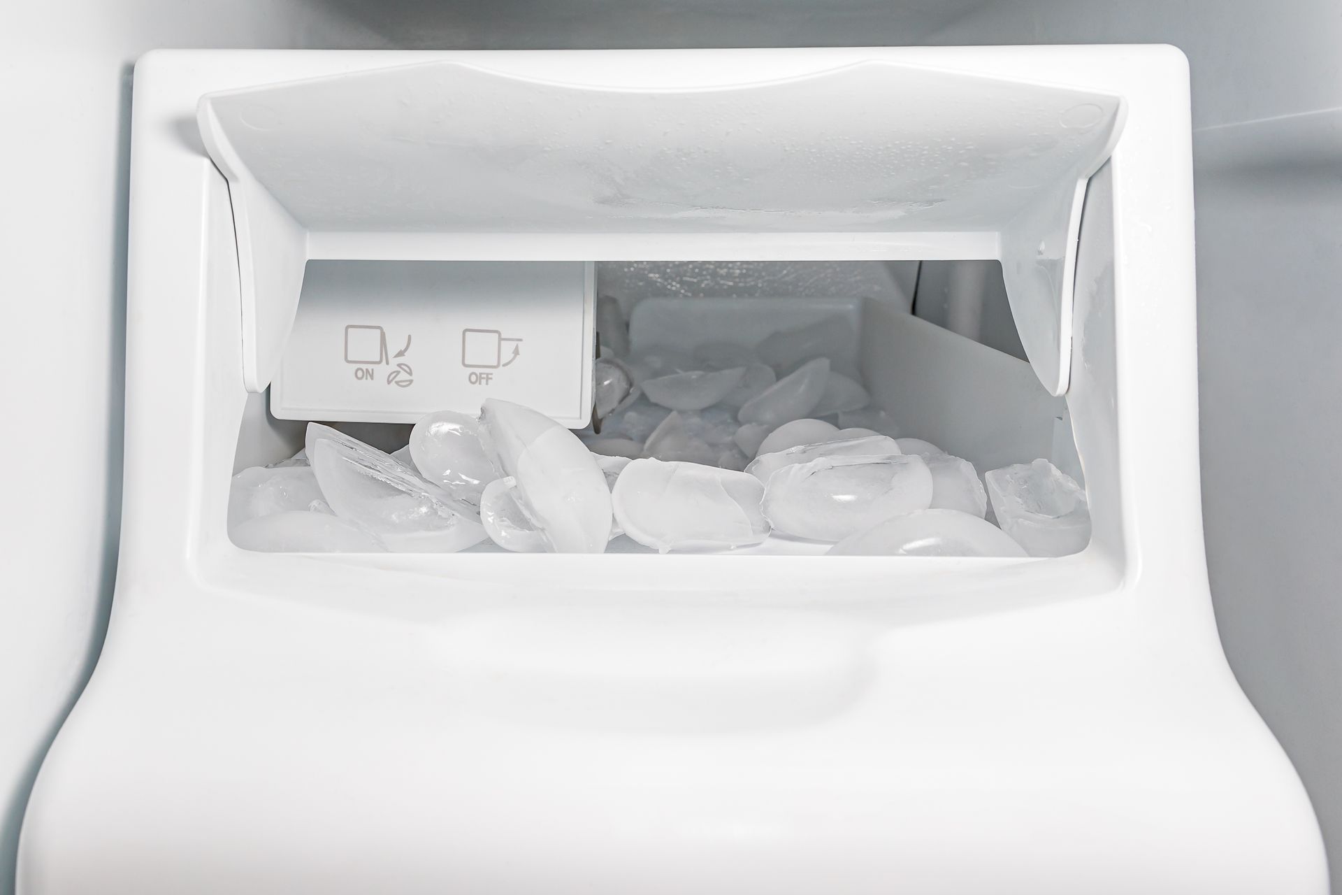 Empty ice maker compartment with scattered ice cubes inside a white freezer.