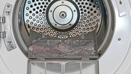 Open dryer with lint-covered clothes inside the drum