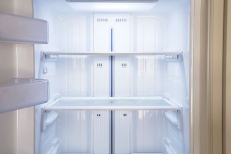Empty white refrigerator interior with glass shelves and door bins