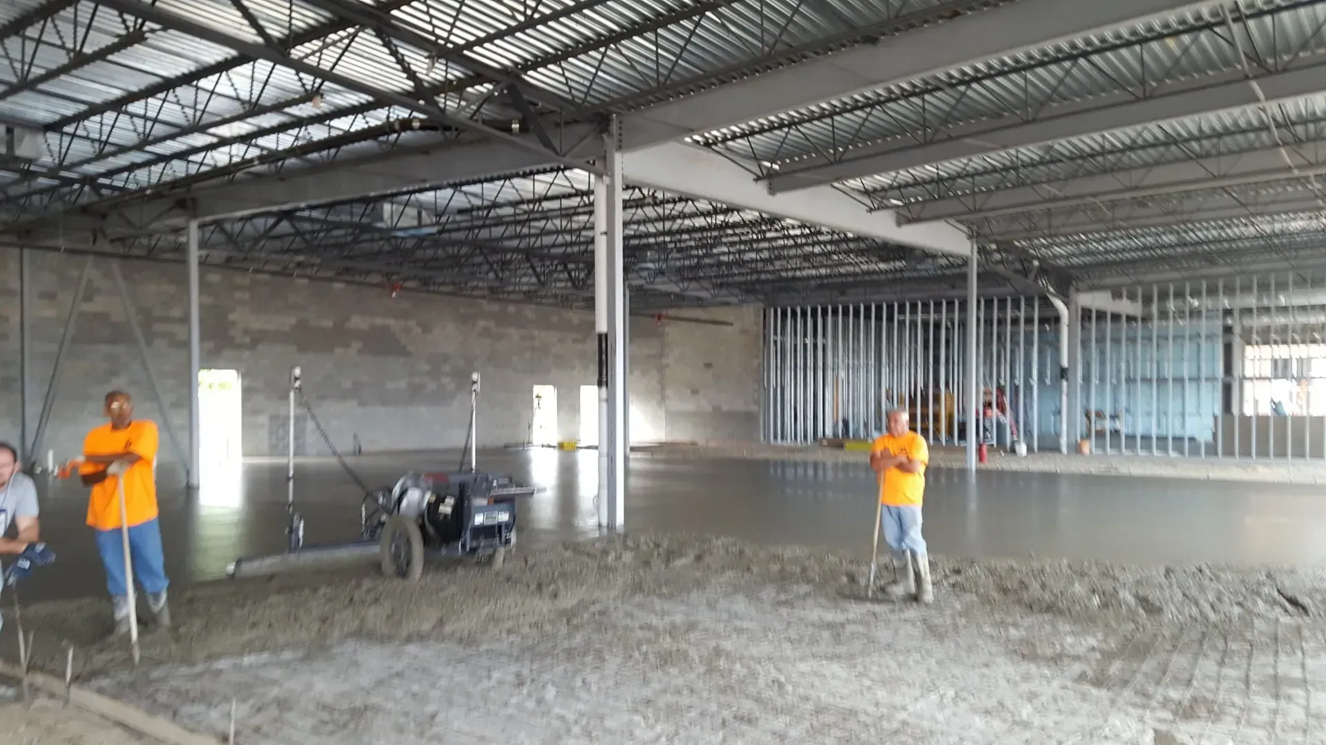 Construction workers leveling wet concrete inside a large unfinished building Construction workers leveling wet concrete inside a large unfinished building