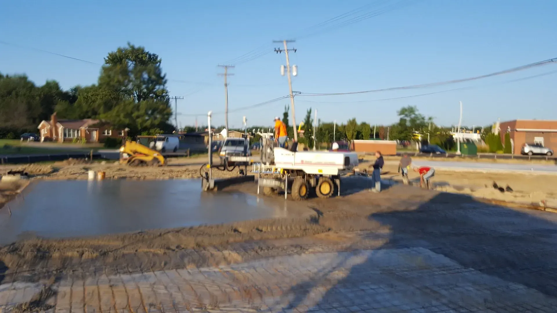 Construction crew paving a road beside a large muddy water pit, with trucks and equipment at sunset Construction crew paving a road beside a large muddy water pit, with trucks and equipment at sunset