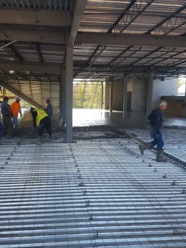 Construction workers in a partially built interior, standing on corrugated metal flooring.