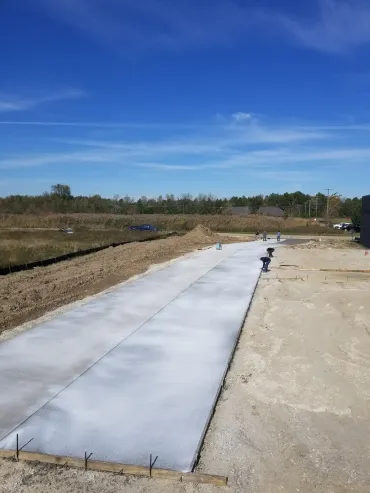 Concrete slab foundation under construction on a cleared site with blue sky and trees in the background