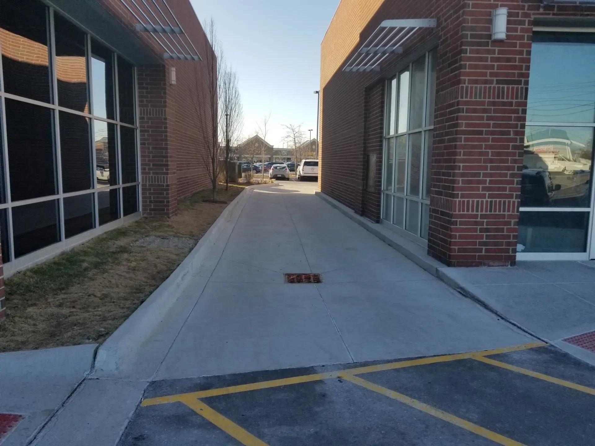 Brick building walkway with a concrete ramp between windows and a parking area. Brick building walkway with a concrete ramp between windows and a parking area.