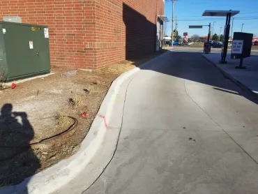 Curved sidewalk beside a brick building with utility boxes, leading toward a sunny street.