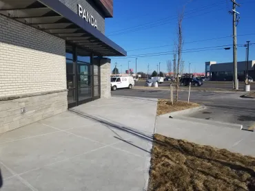 Front of a commercial building with sidewalk, parking lot, and clear blue sky