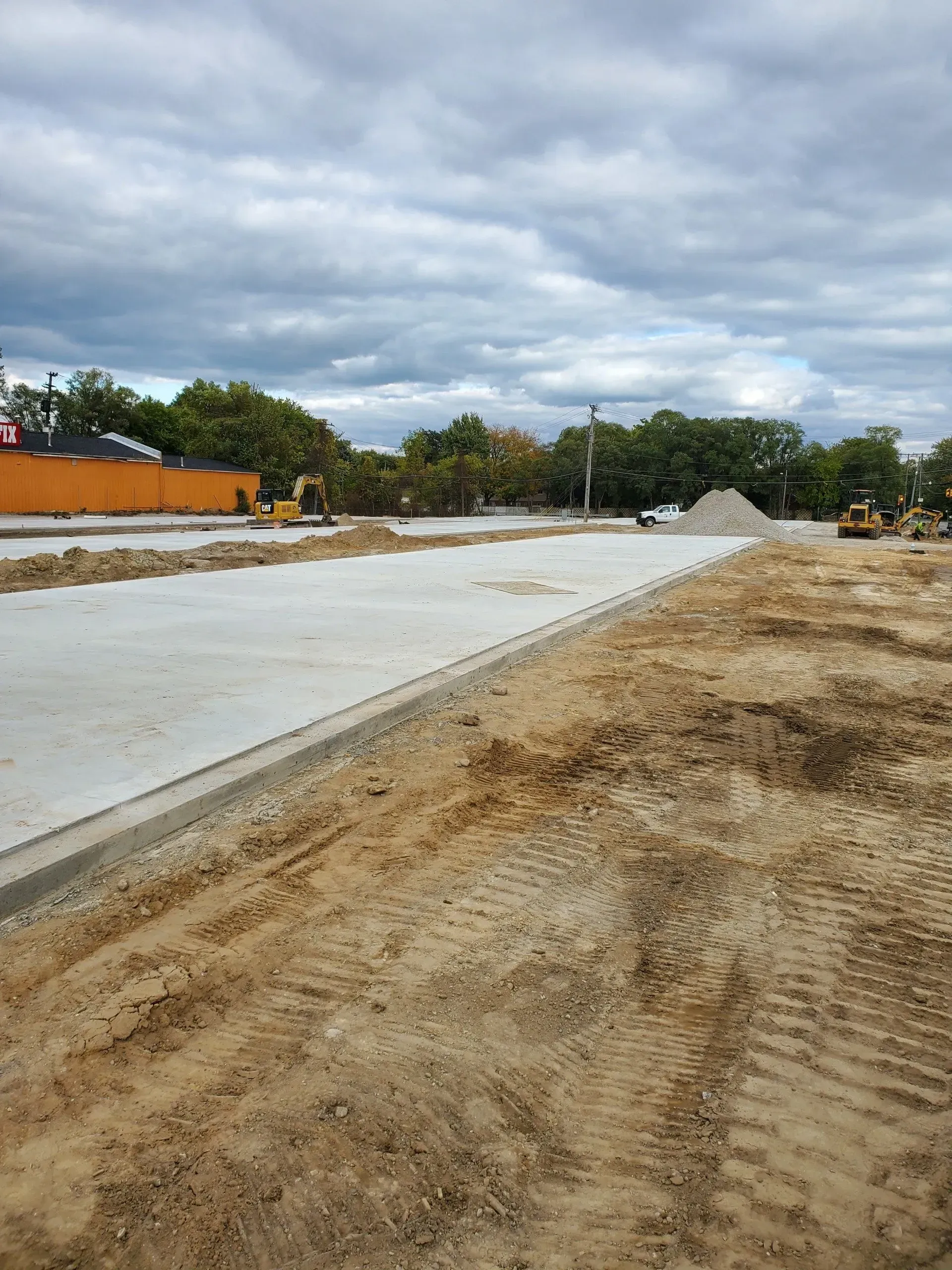 Construction site with concrete slab, dirt road, and piles of gravel under cloudy sky Construction site with concrete slab, dirt road, and piles of gravel under cloudy sky