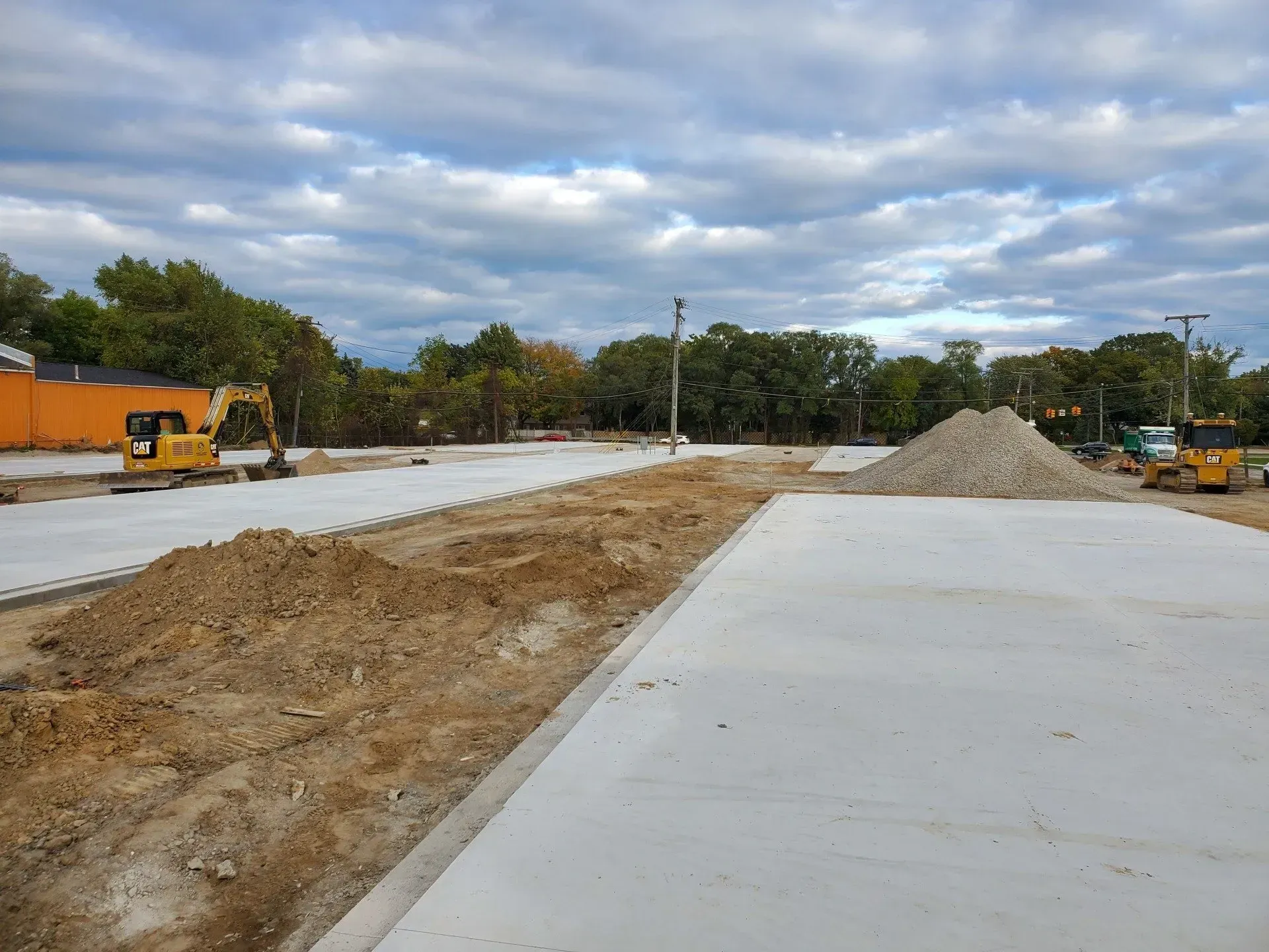 Construction site with new concrete road, dirt piles, and heavy equipment under cloudy sky
