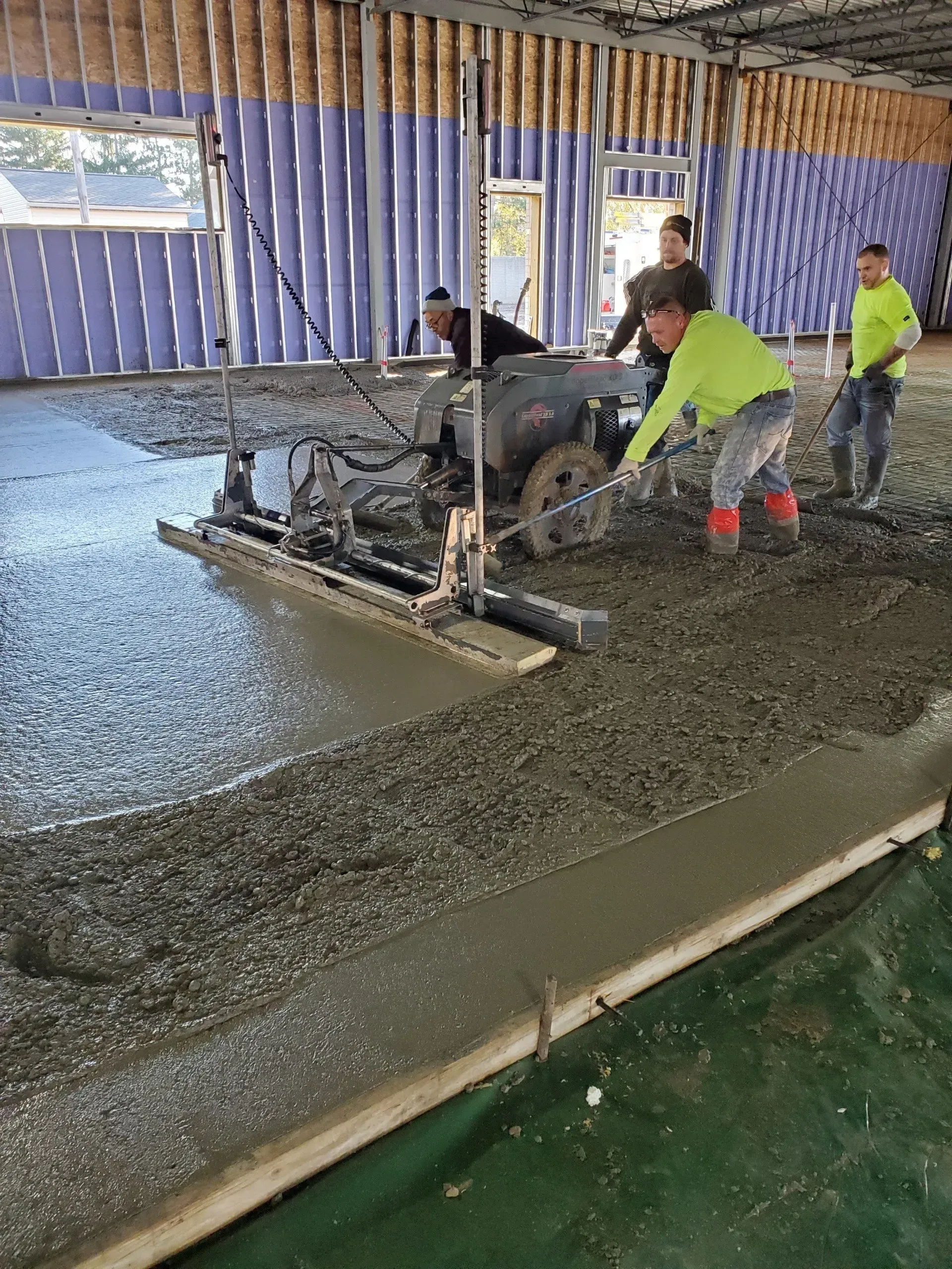 Workers pouring and smoothing wet concrete indoors with a power screed in a construction area. Workers pouring and smoothing wet concrete indoors with a power screed in a construction area.
