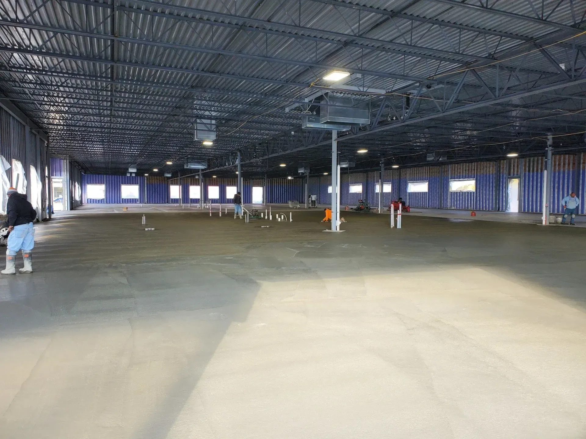 Empty indoor warehouse with a high metal ceiling and a few people standing near the far wall