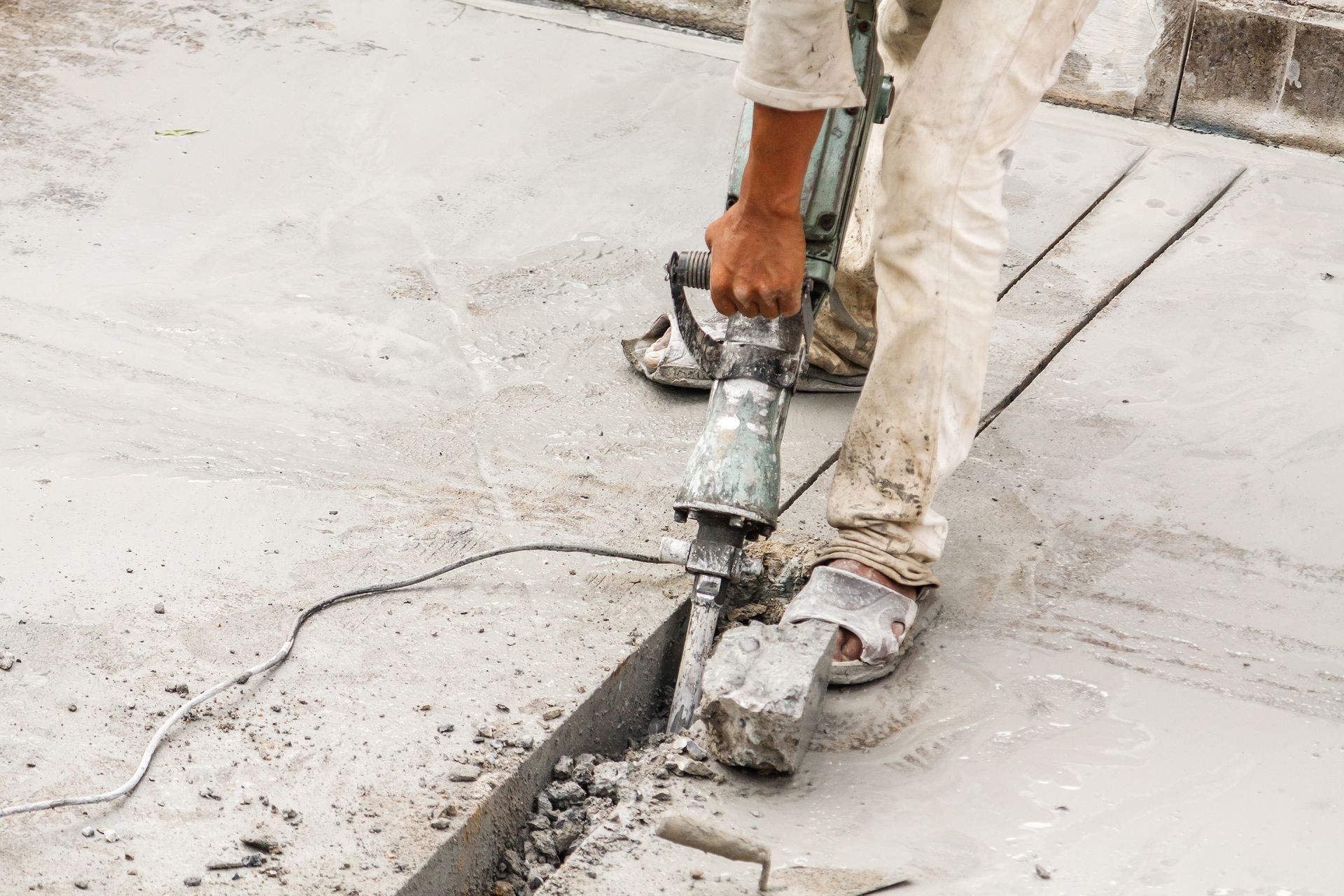 Worker using a power tool to cut or break concrete pavement outdoors Worker using a power tool to cut or break concrete pavement outdoors