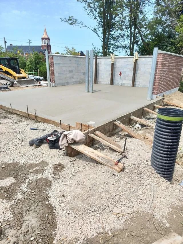 Concrete foundation under construction with brick walls, wooden formwork, and a black drainage pipe in the foreground Concrete foundation under construction with brick walls, wooden formwork, and a black drainage pipe in the foreground