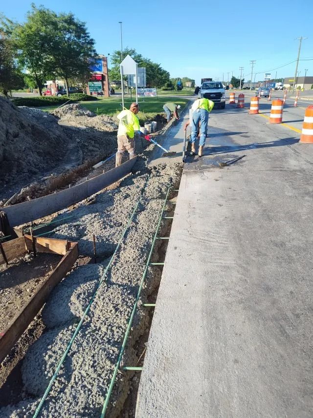 Roadside construction workers laying gravel beside a paved street with orange traffic barrels Roadside construction workers laying gravel beside a paved street with orange traffic barrels