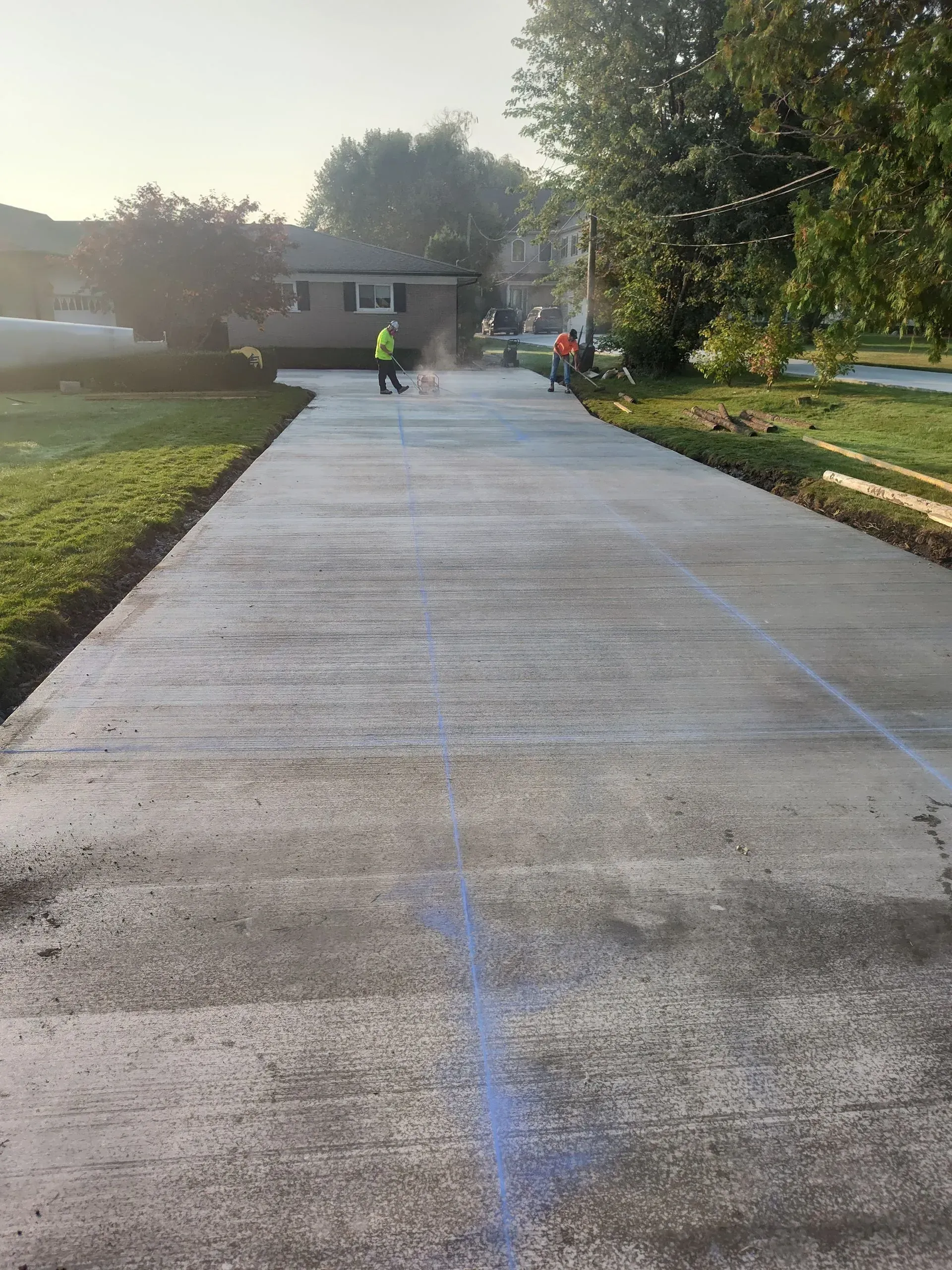 New concrete walkway under construction with workers and trees in a park-like setting
