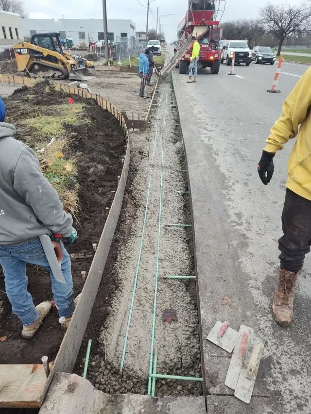 Roadwork crew digging a long trench beside a street with workers and heavy equipment on a gray day Roadwork crew digging a long trench beside a street with workers and heavy equipment on a gray day