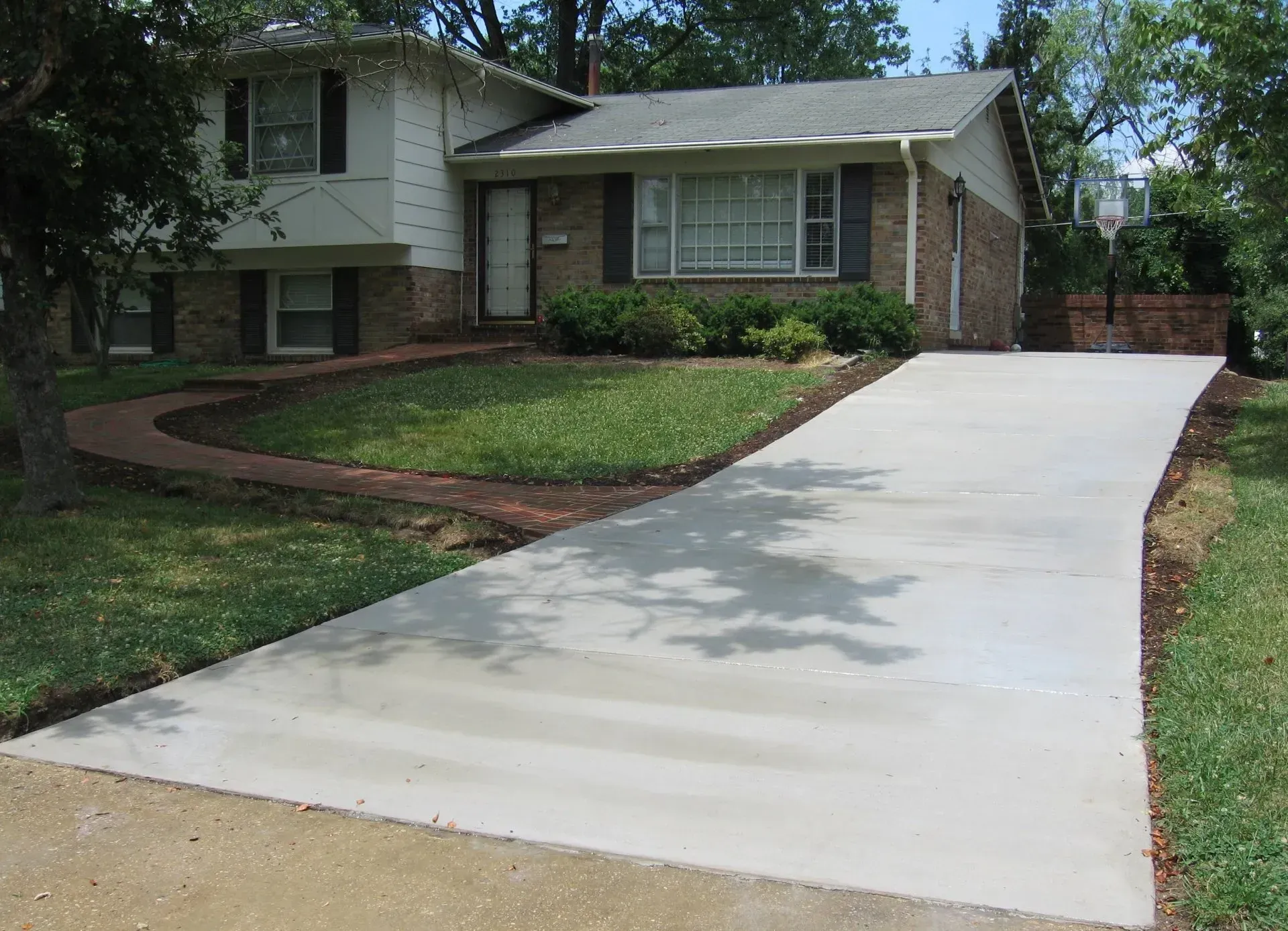 Residential driveway with a smooth light-gray concrete slab leading to a brick house and garage. Residential driveway with a smooth light-gray concrete slab leading to a brick house and garage.