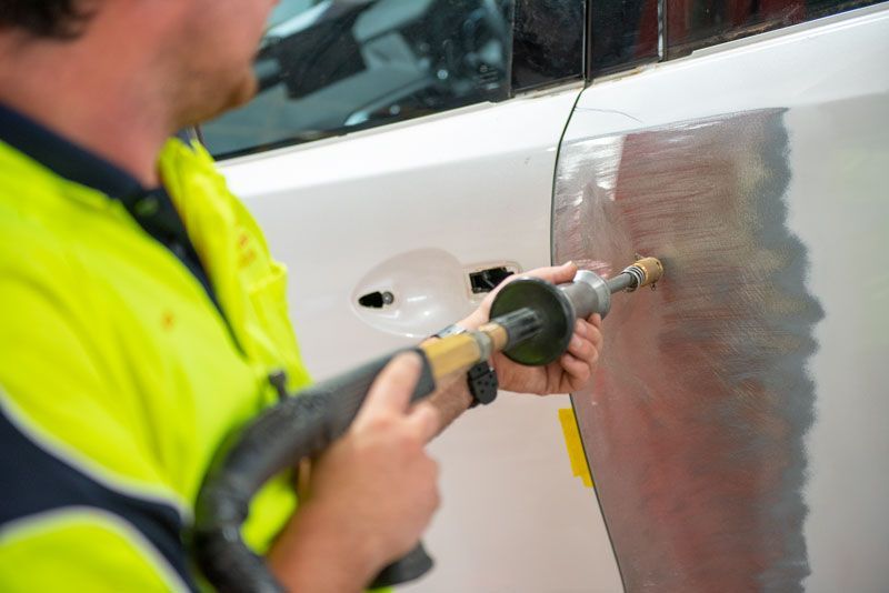 A man is working on a car door with a tool.