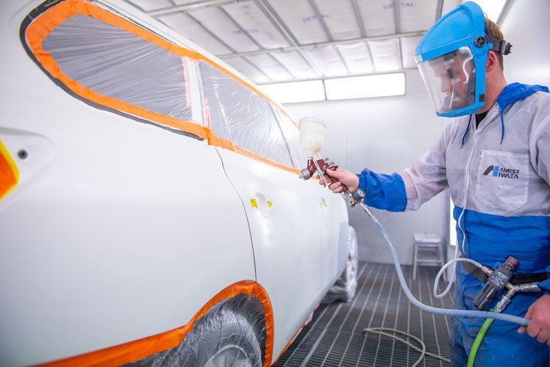A man is spray painting a white car in a paint booth.