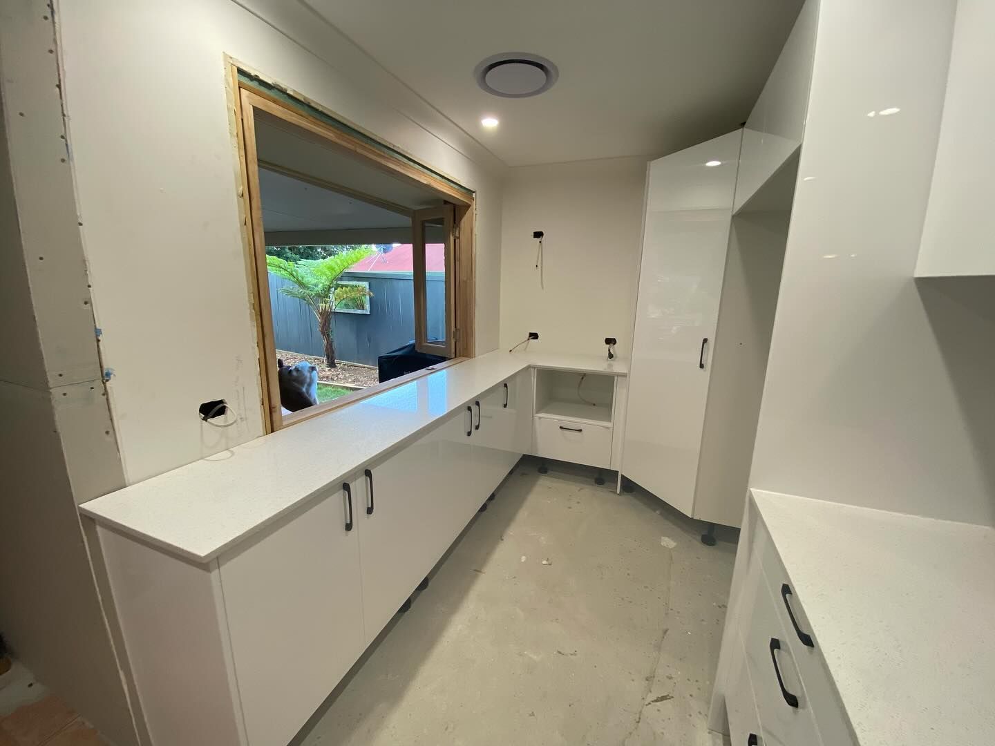 White kitchen cabinets installed, with a window and unfinished walls.
