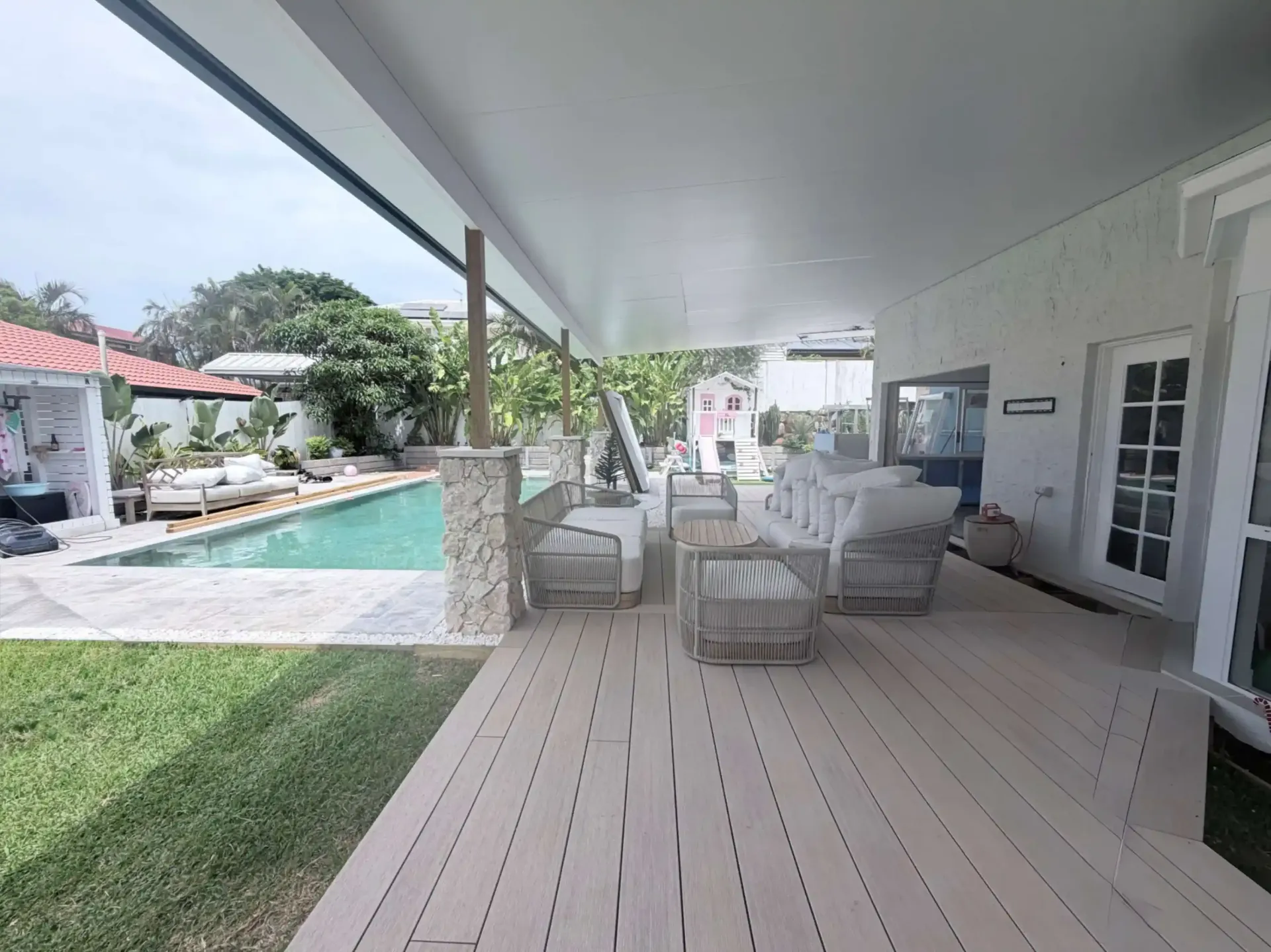 Covered outdoor patio with seating overlooking a pool and yard.