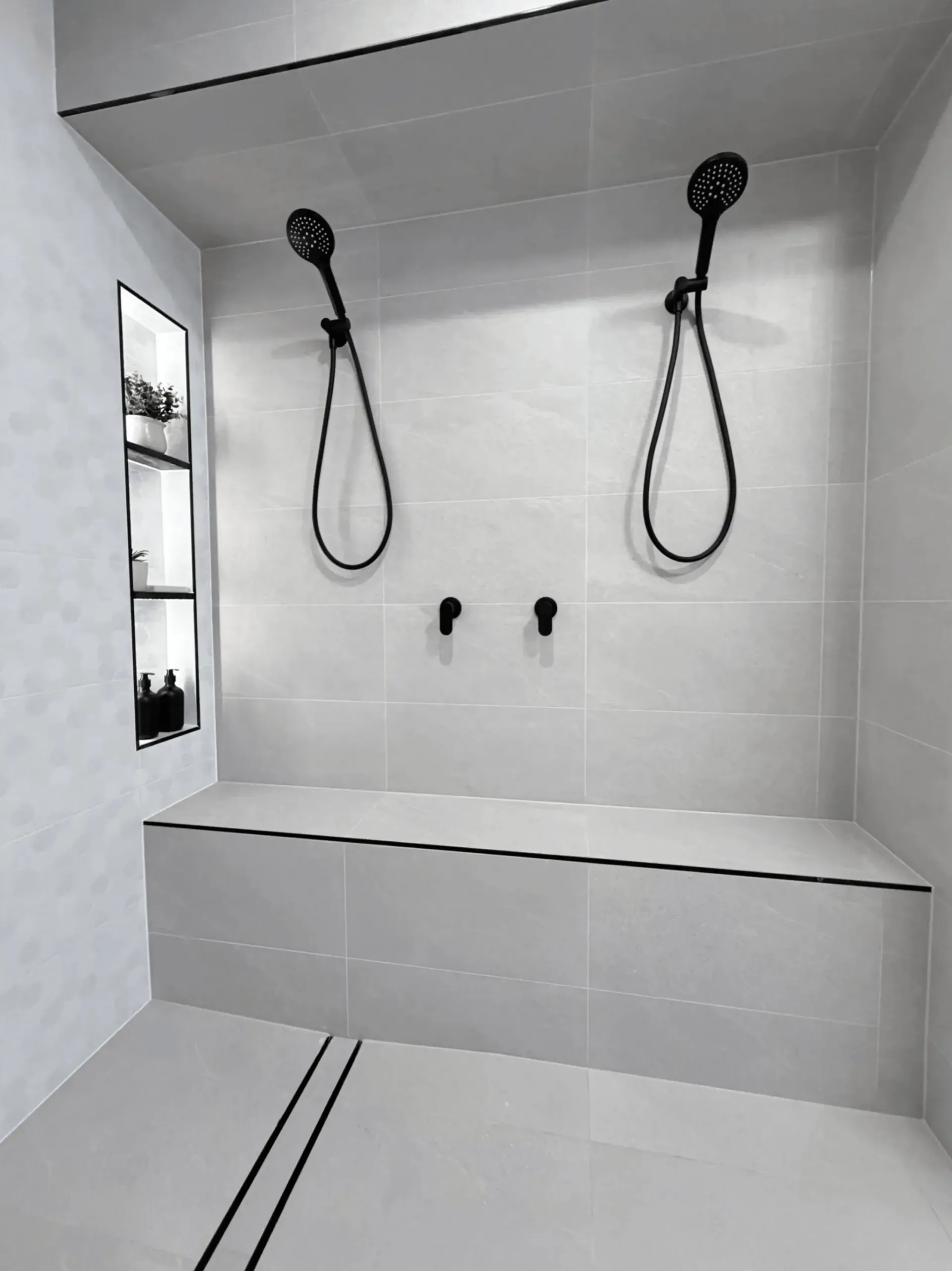 Modern, tiled shower with two black showerheads, bench, and built-in shelving. Gray tones dominate.