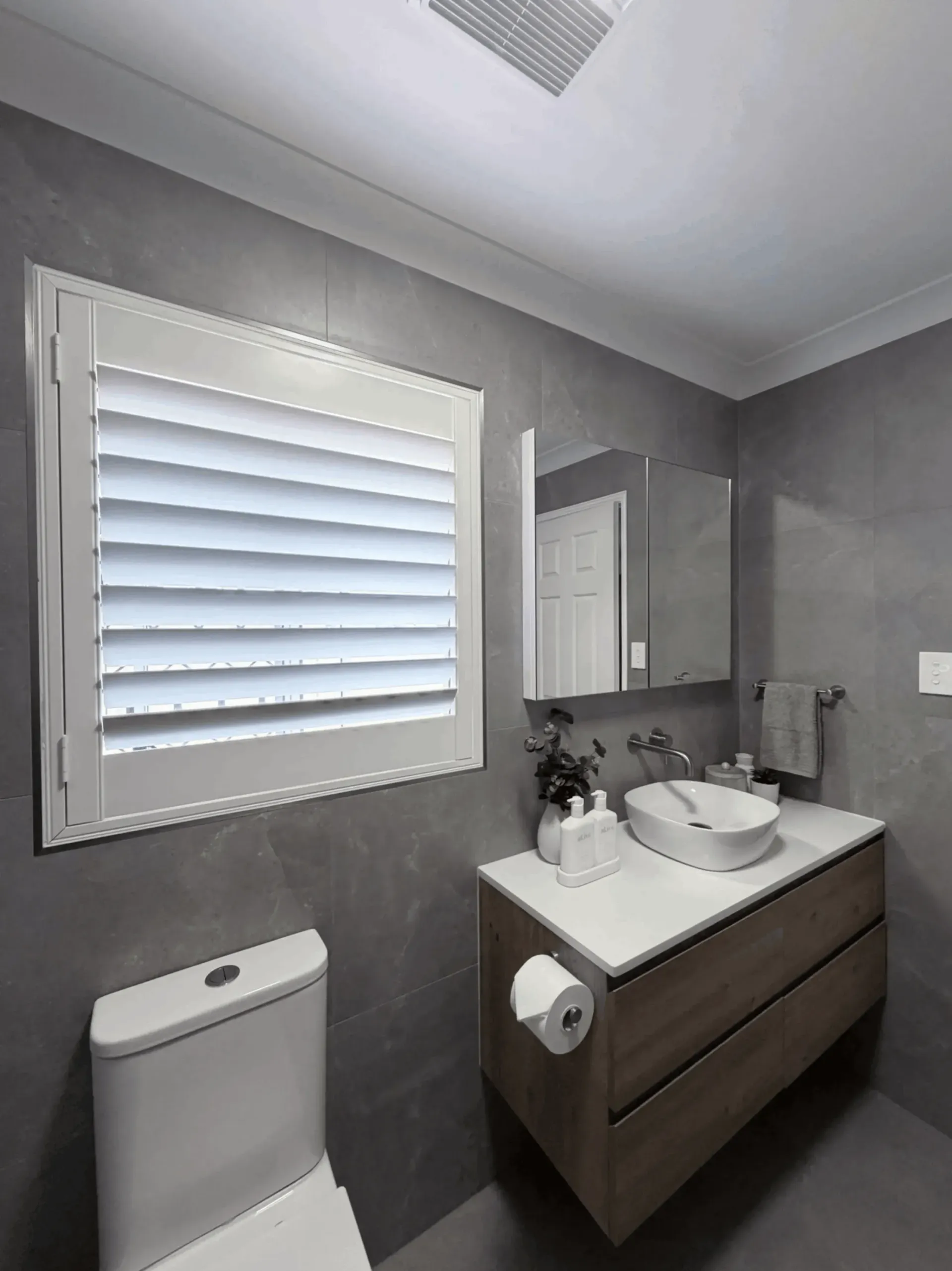 Bathroom with a toilet, vanity with a vessel sink, window with shutters, and gray walls.