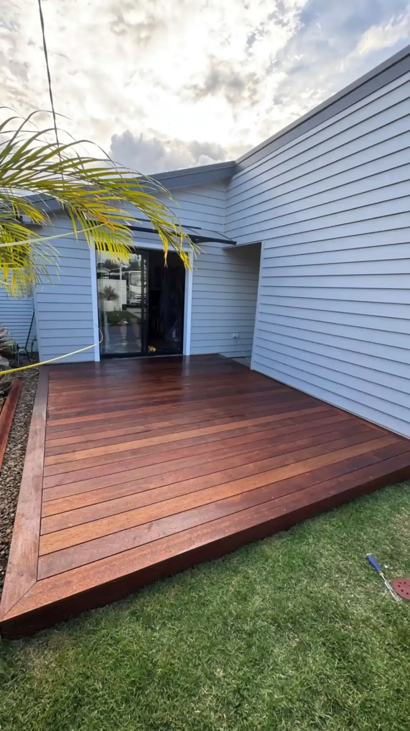 Wooden deck against a gray building with sliding glass doors, on a grassy lawn.
