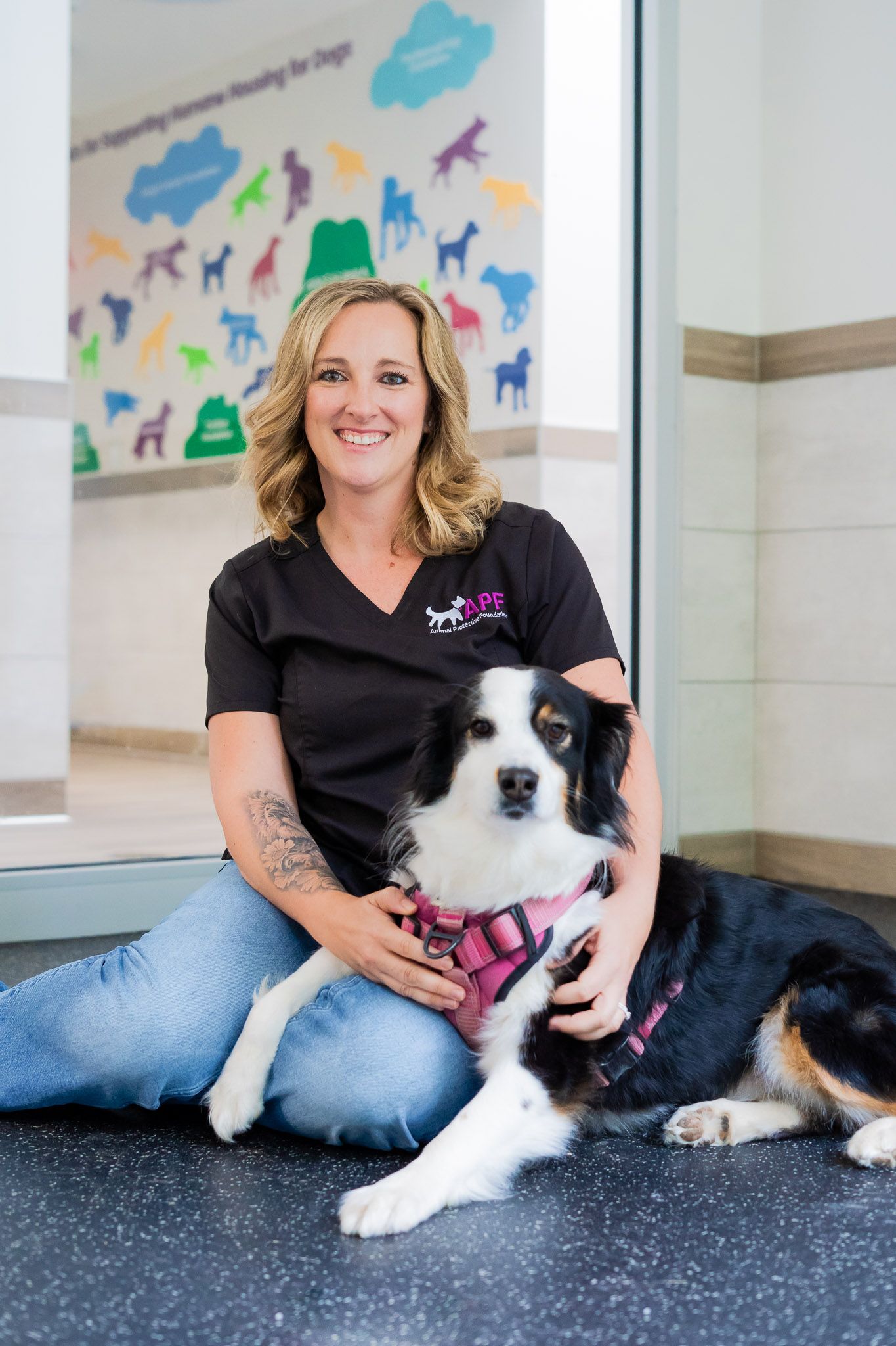 A woman is kneeling down next to a dog on the floor.