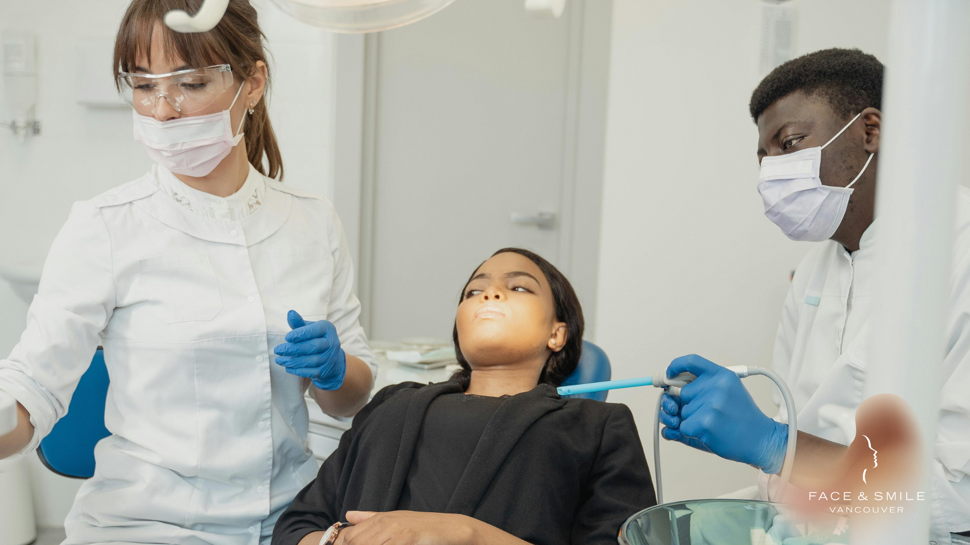 A woman is sitting in a dental chair getting her teeth examined by two dentists.
