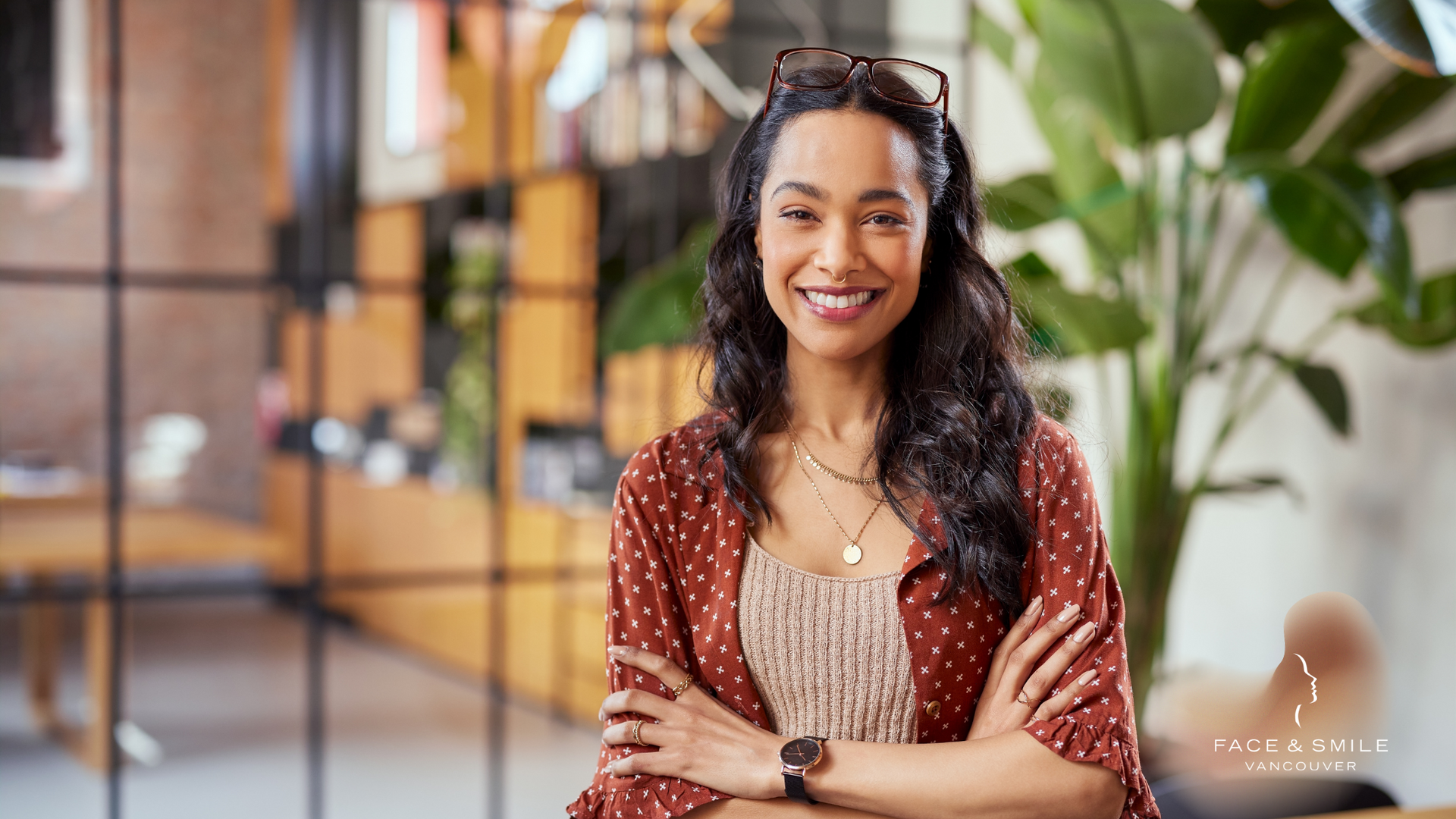 A woman is smiling with her arms crossed in an office.