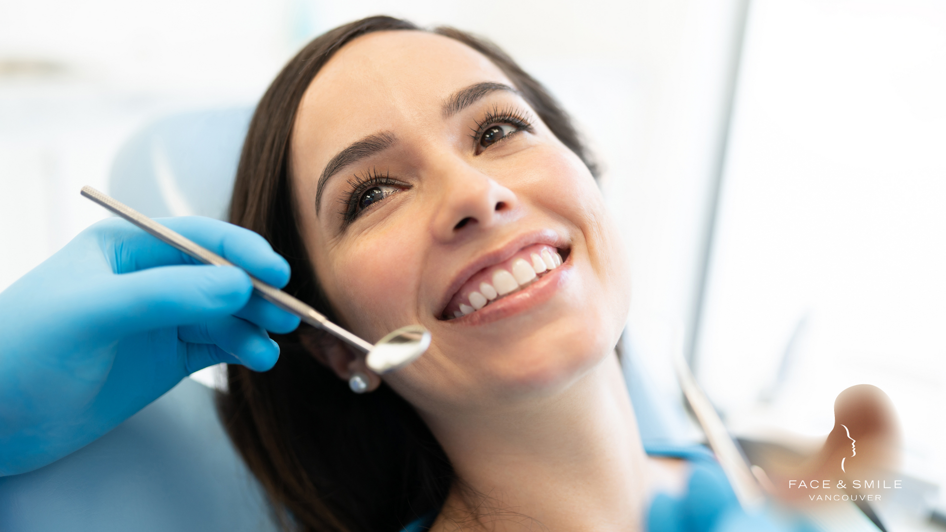 Dental patient smiling while dentist examines her teeth with a mirror and gloved hands