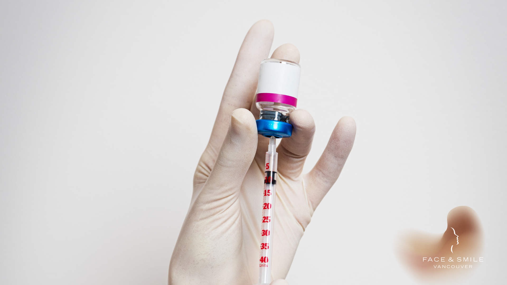 A person in a glove is holding a syringe and a bottle of vaccine.