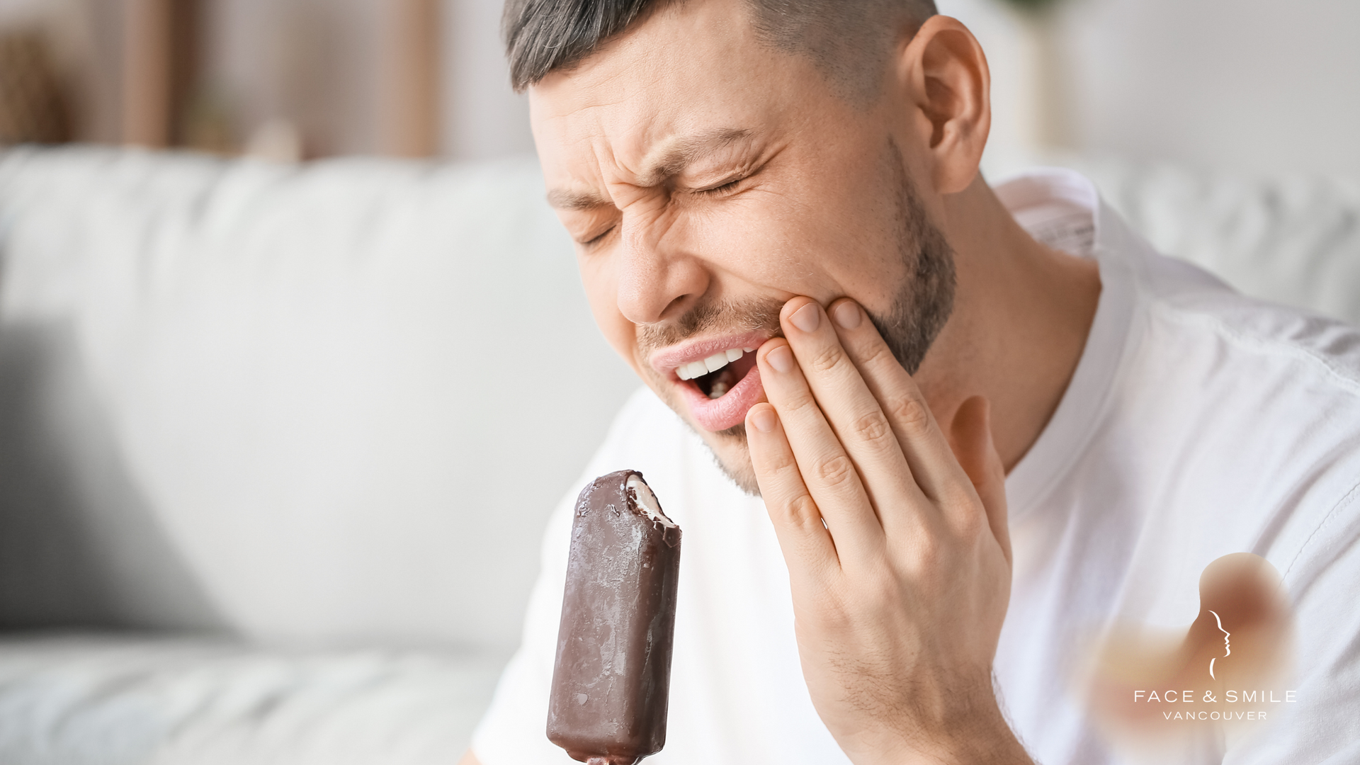 A man is eating an ice cream bar and has a toothache.