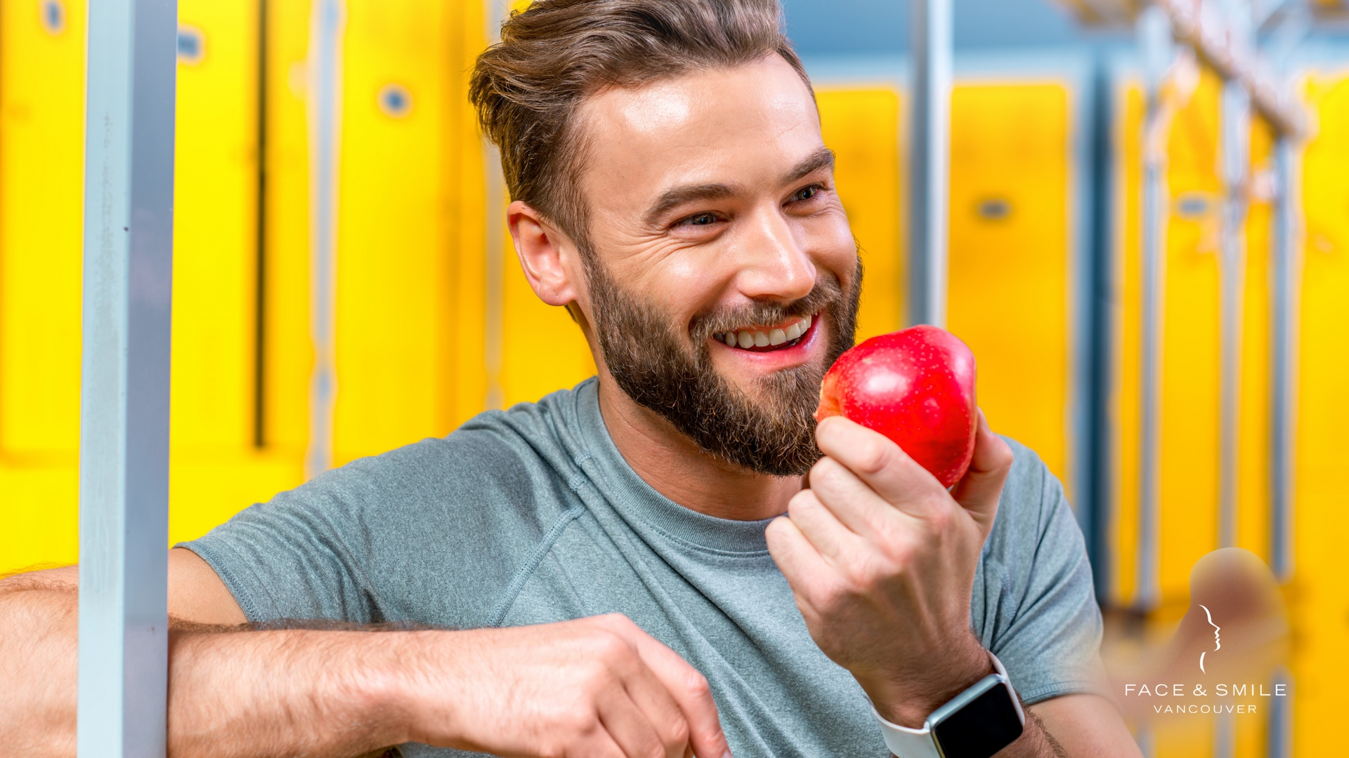 Smiling man holding a red apple in a bright gym or fitness studio
