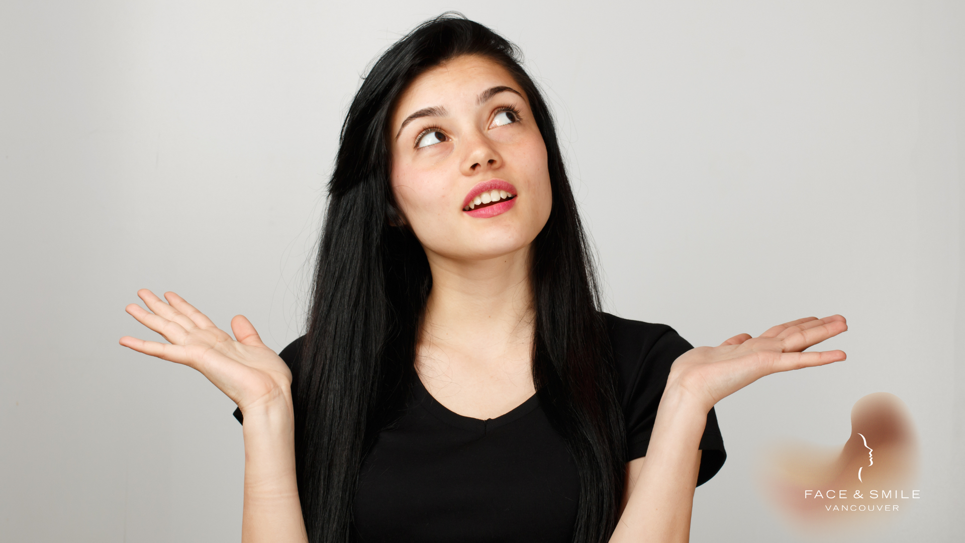 Woman with long black hair shrugging with palms up, looking upward against a light gray background.