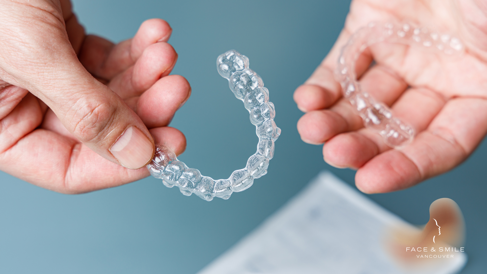 Hands holding a clear dental aligner on a light blue background