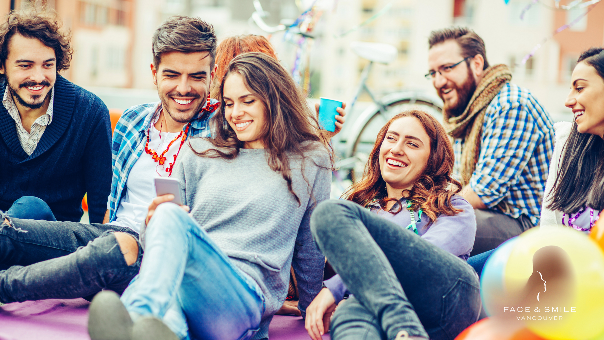 Group of smiling friends sitting together outdoors, laughing and chatting in casual clothes.