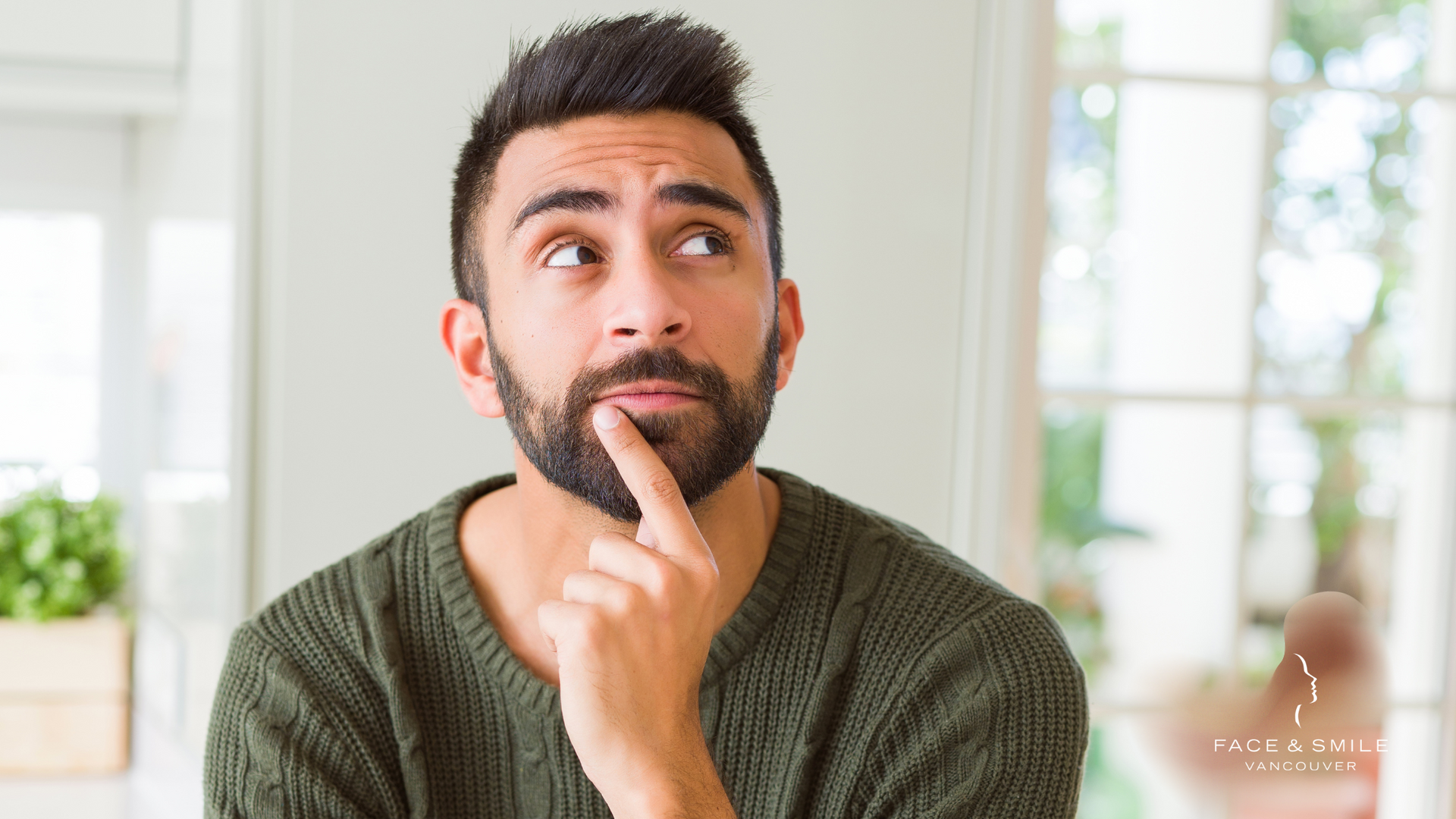 A man with a beard is holding his finger to his chin and looking up.