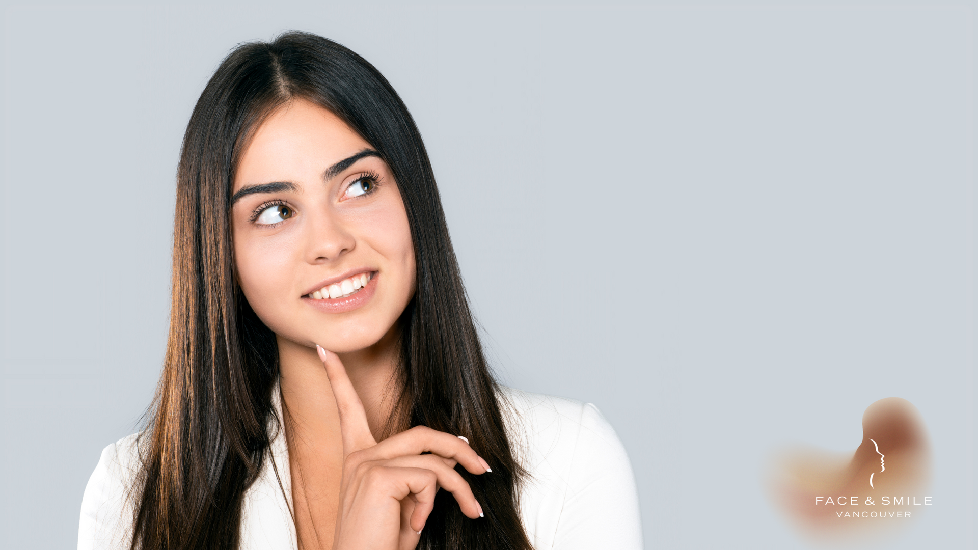 A woman with long hair is smiling and looking up while holding her hand to her chin.